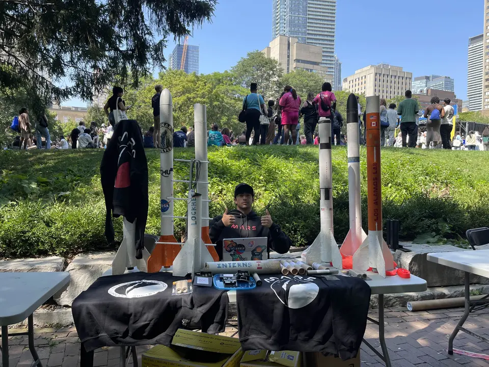 Students and model rockets displayed together at an outdoor table