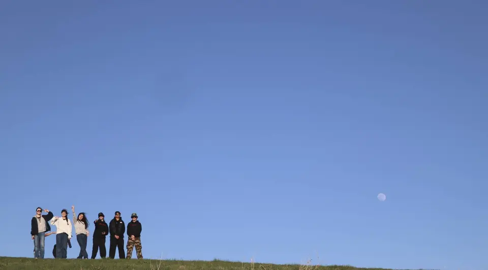 Students standing on a grassy hill beneath a blue sky