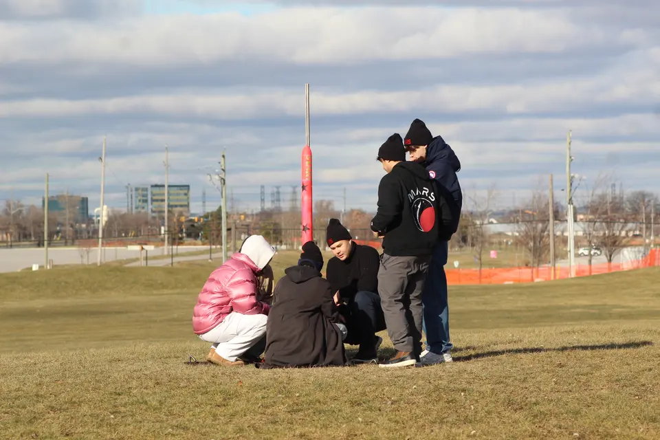Students crouching beside a rocket on the launch field