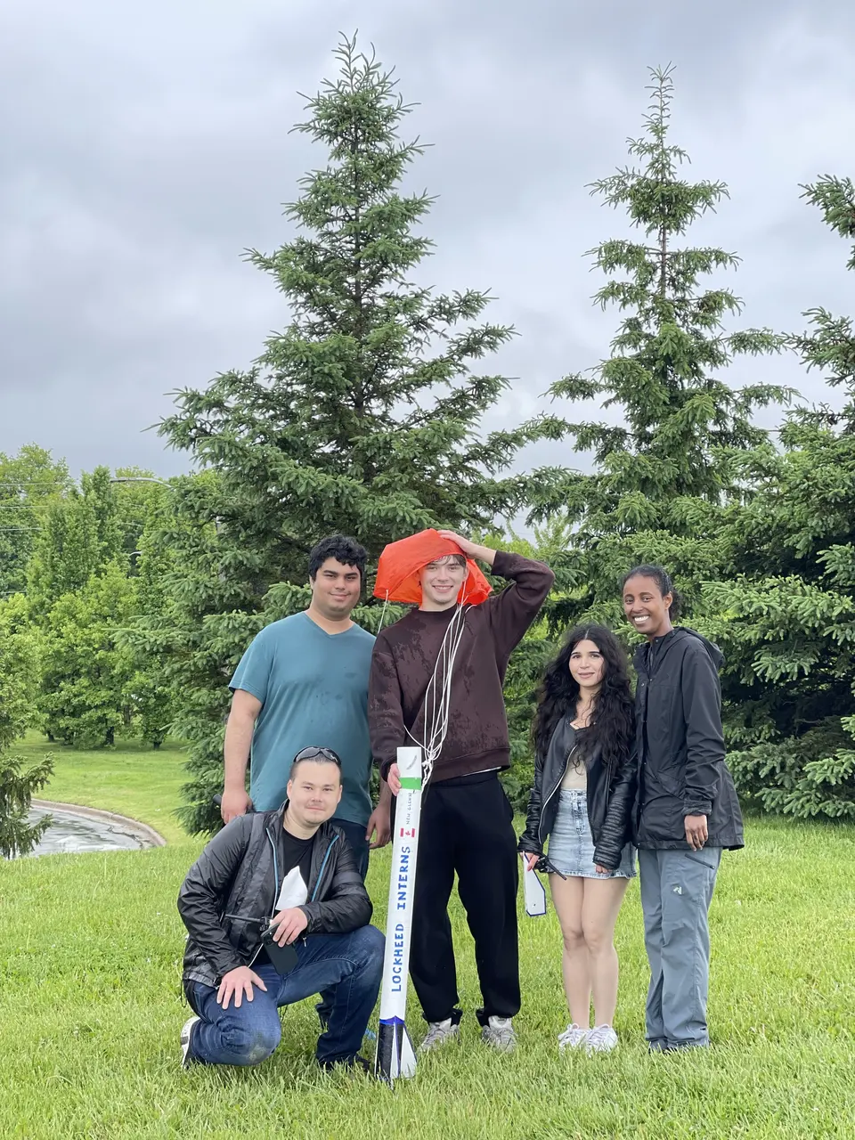 Students standing with their rocket beneath a tree