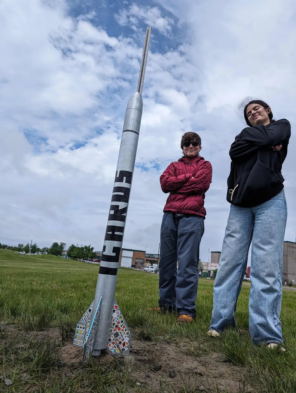 Two students posing beside a tall rocket