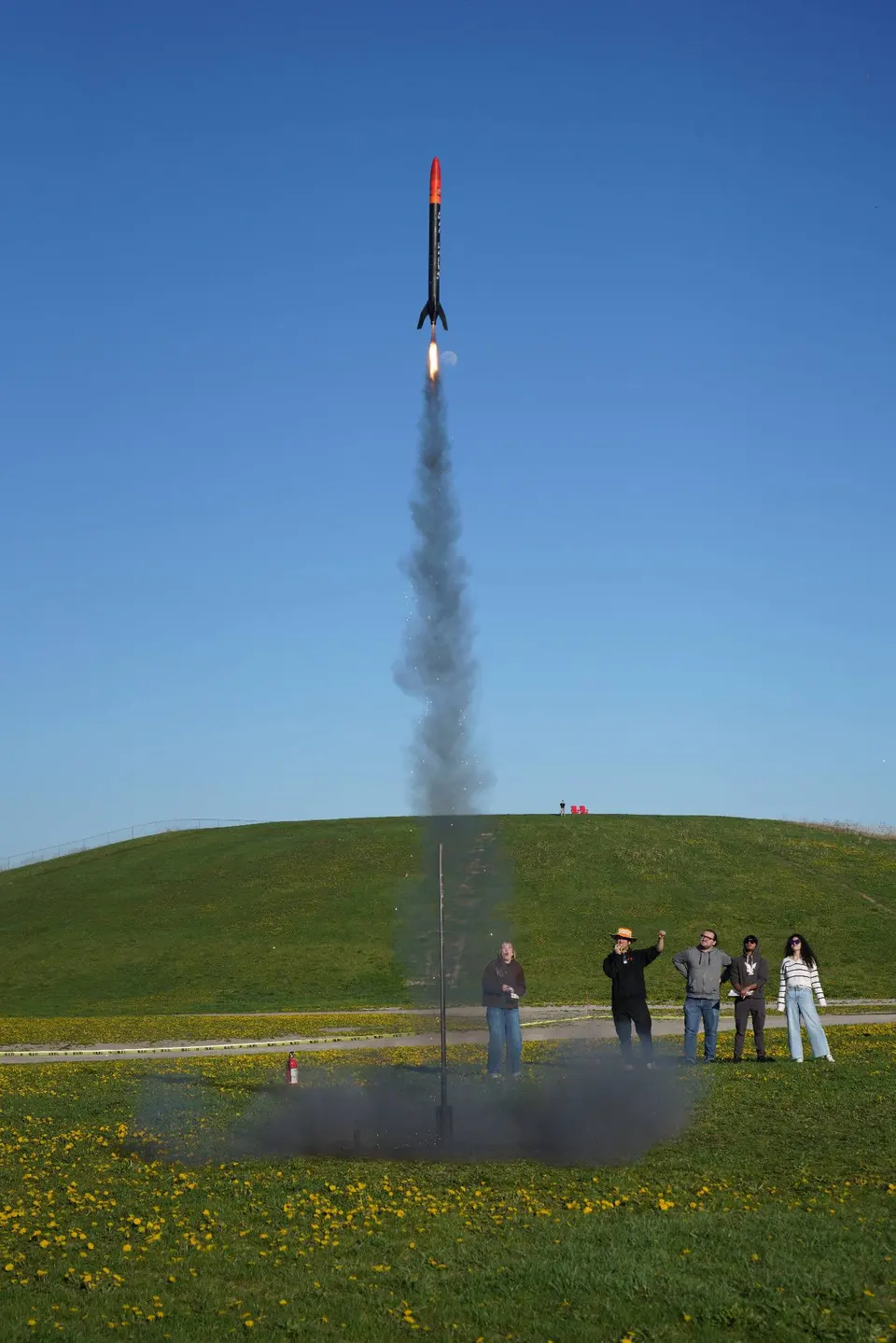 Black rocket with a red nose cone climbing above a launch rod
