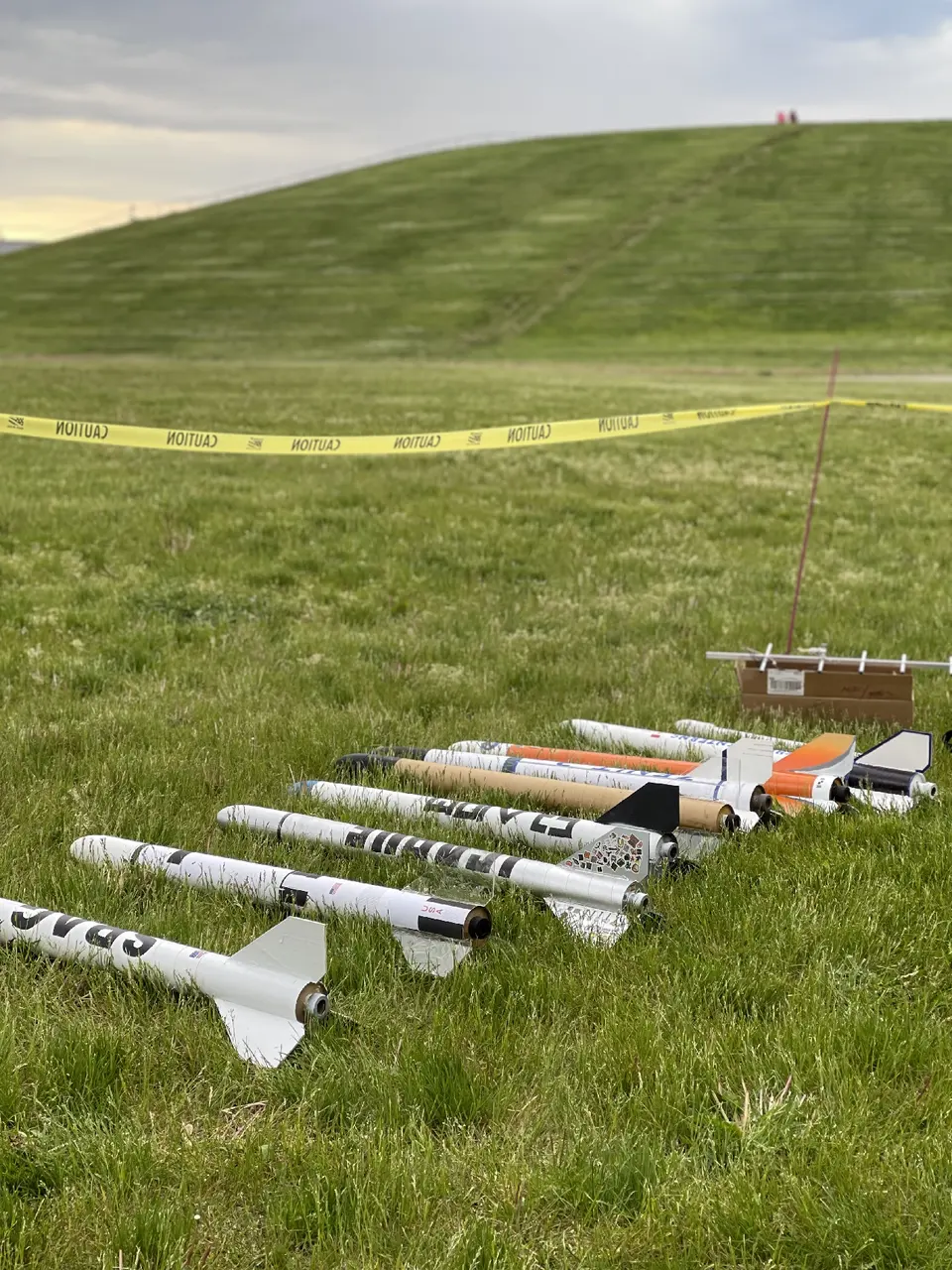 Model rockets lined up on the grass behind safety tape