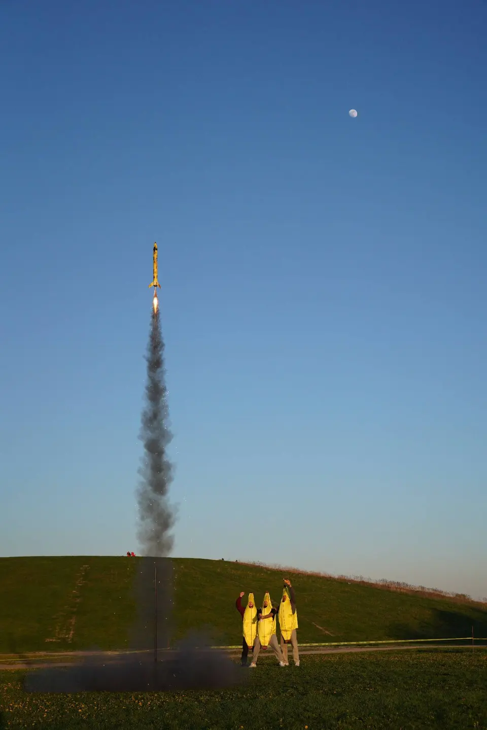 A model rocket rising above the launch field on a smoke plume